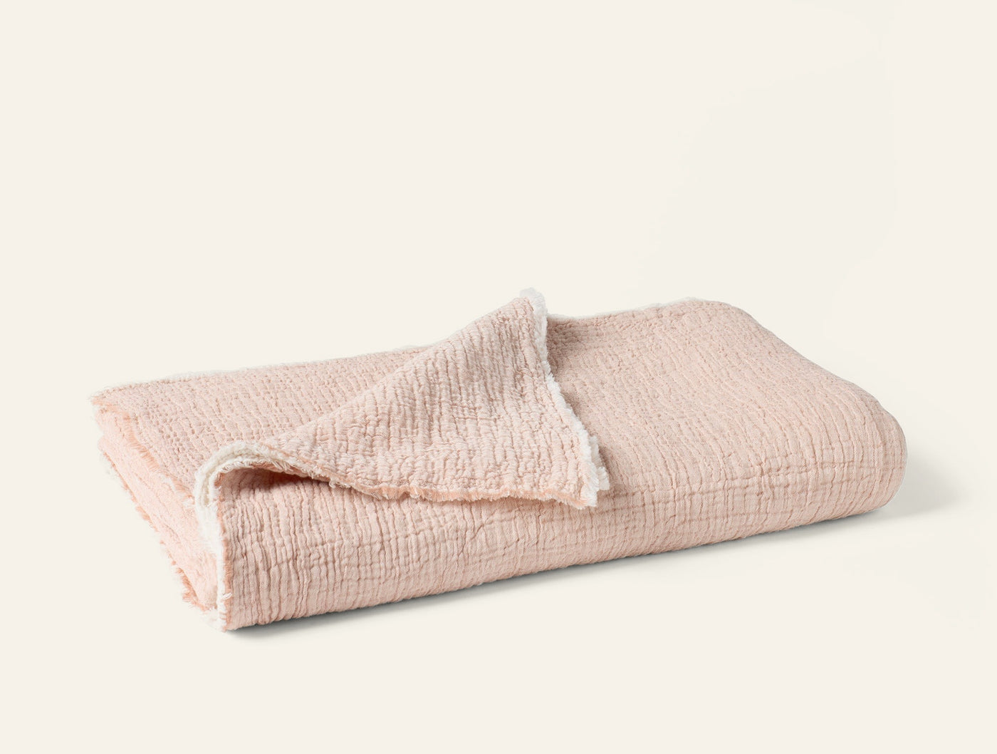 Folded blush Coyuchi Topanga Matelasse throw showing textured crinkle weave and soft edge detail.