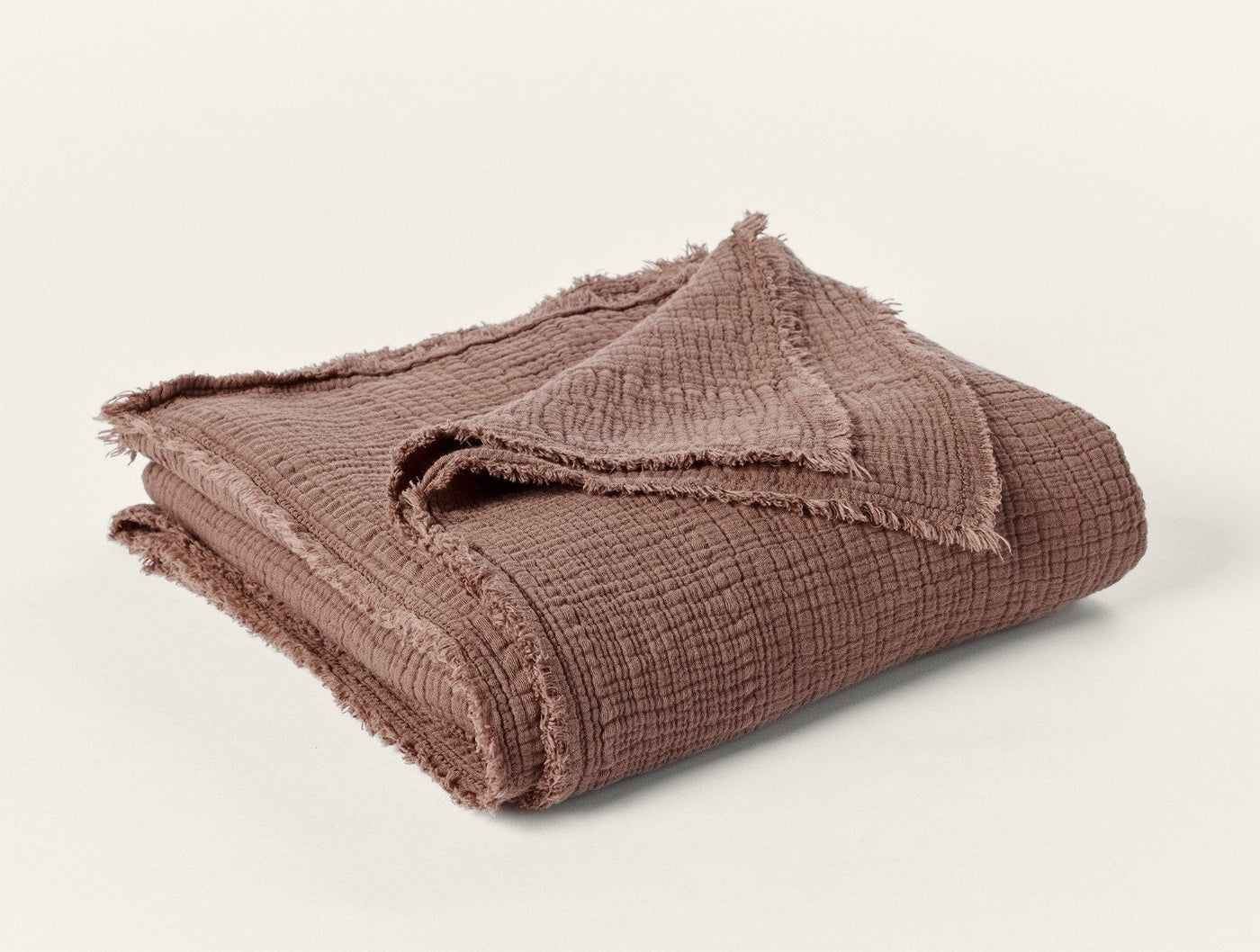 Frayed edge detail on folded Topanga Matelasse throw in warm mauve-brown matelasse weave.