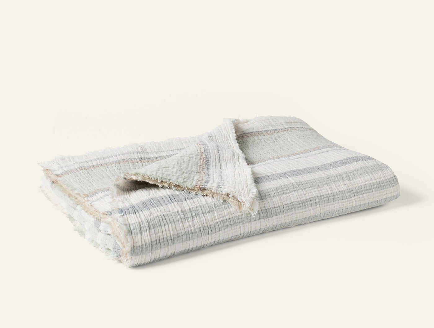 Folded Coyuchi Topanga Matelassé throw in ivory with soft grey stripes and fringe trim.