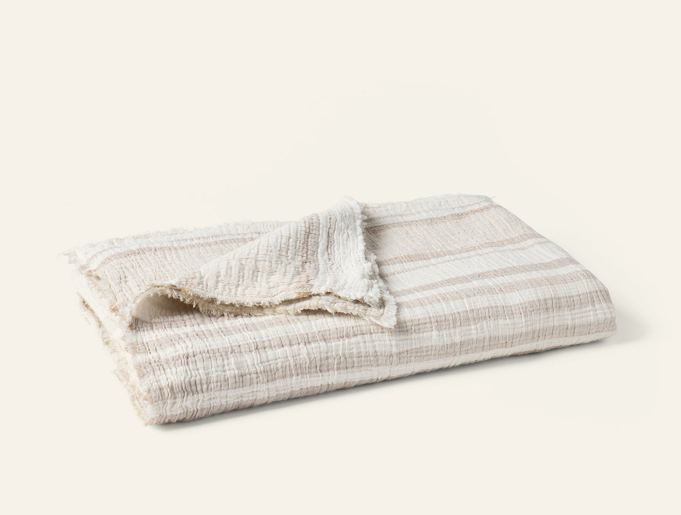 Folded ivory and taupe striped matelasse throw with fringe trim detail.