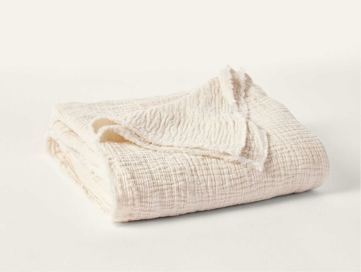 Ivory matelasse throw folded to show crinkled texture and fringe edge detail.