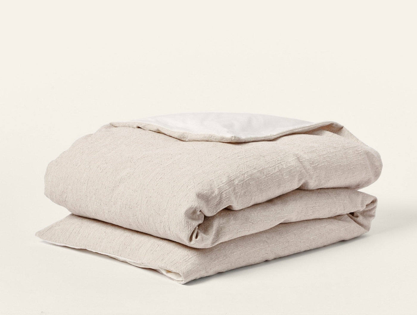 Folded oatmeal linen duvet cover showing natural texture and ivory interior contrast.