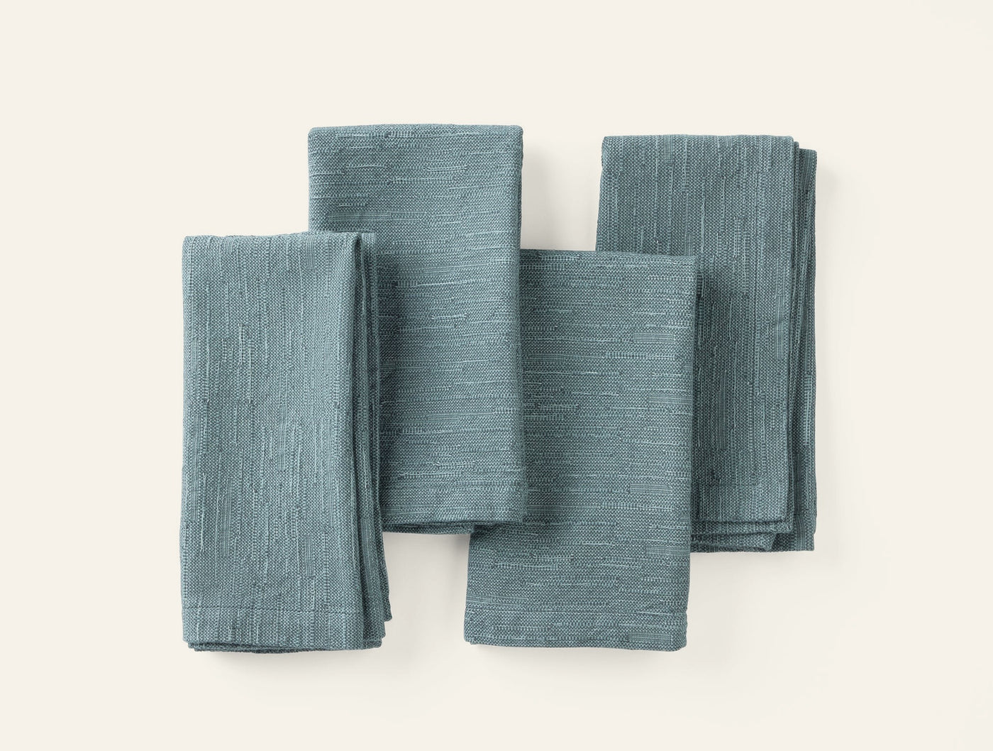 Four folded Coyuchi Toro Canyon napkins in slate blue linen, arranged in a flat lay on white.