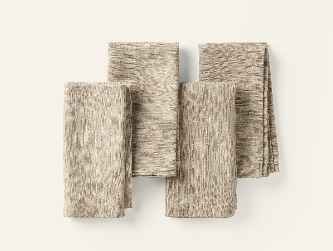 Four folded Coyuchi Toro Canyon linen napkins in natural tan, arranged flat on white surface.