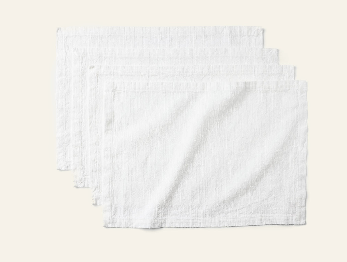 Coyuchi Toro Canyon placemats in white, set of four fanned on grey background.