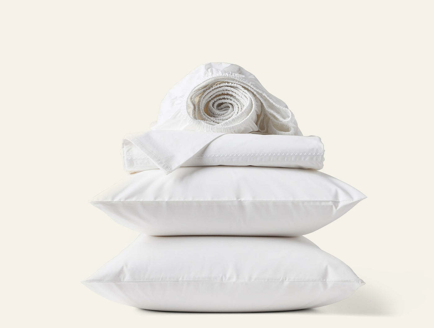 Coyuchi Trailing Embroidered sheet set in white, stacked with pillows and rolled linens.