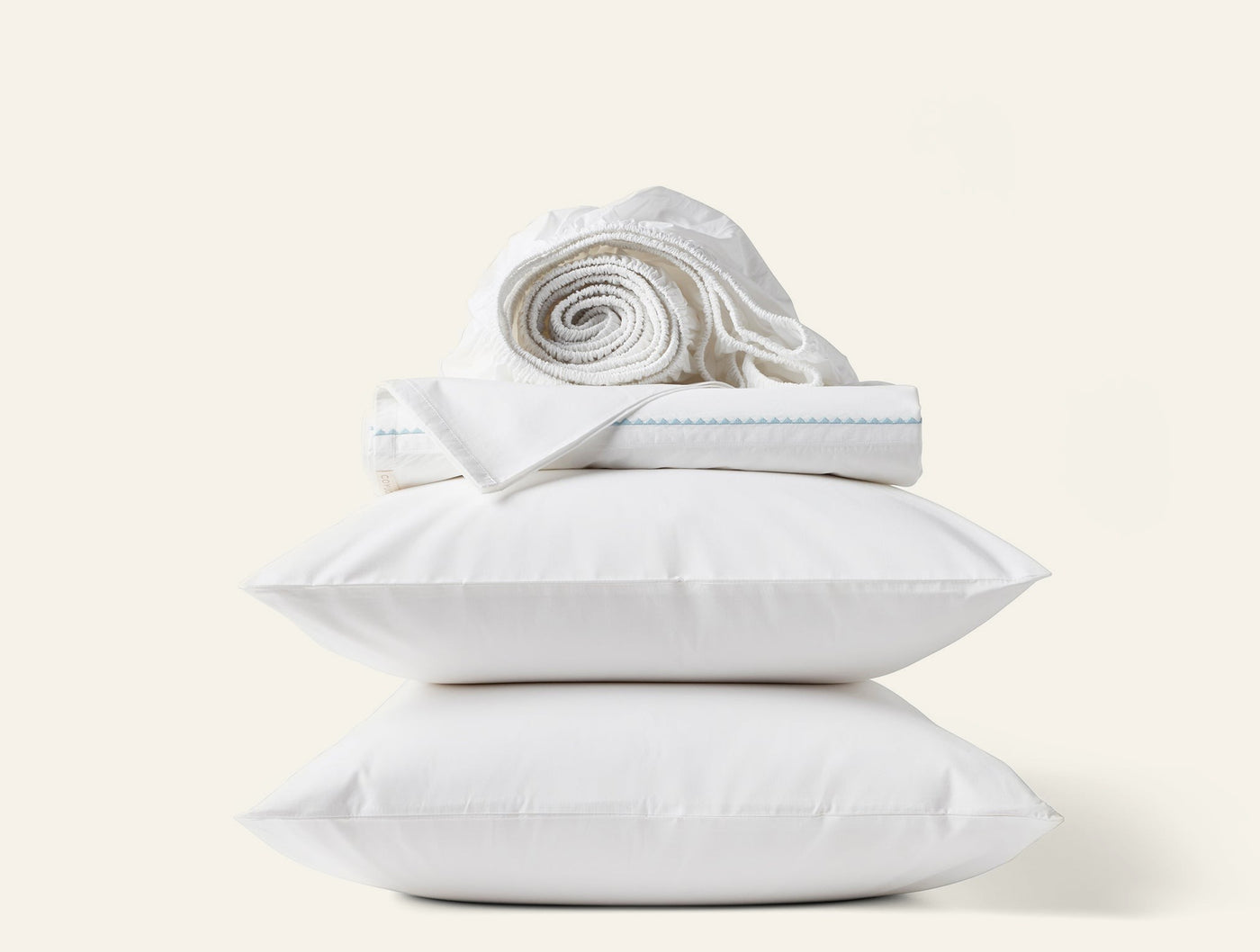 Close-up of two stacked white pillows with folded Coyuchi sheets and a rolled flat sheet on top.