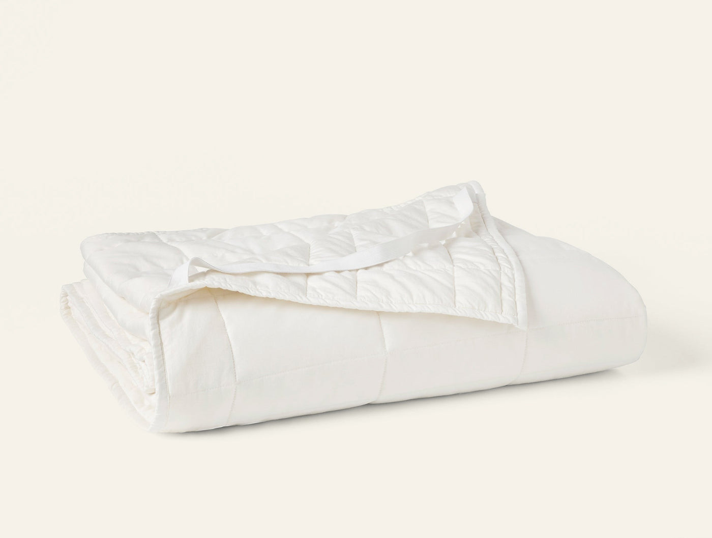 Coyuchi Washable Wool Filled Mattress Topper in white, neatly folded showing quilted texture.