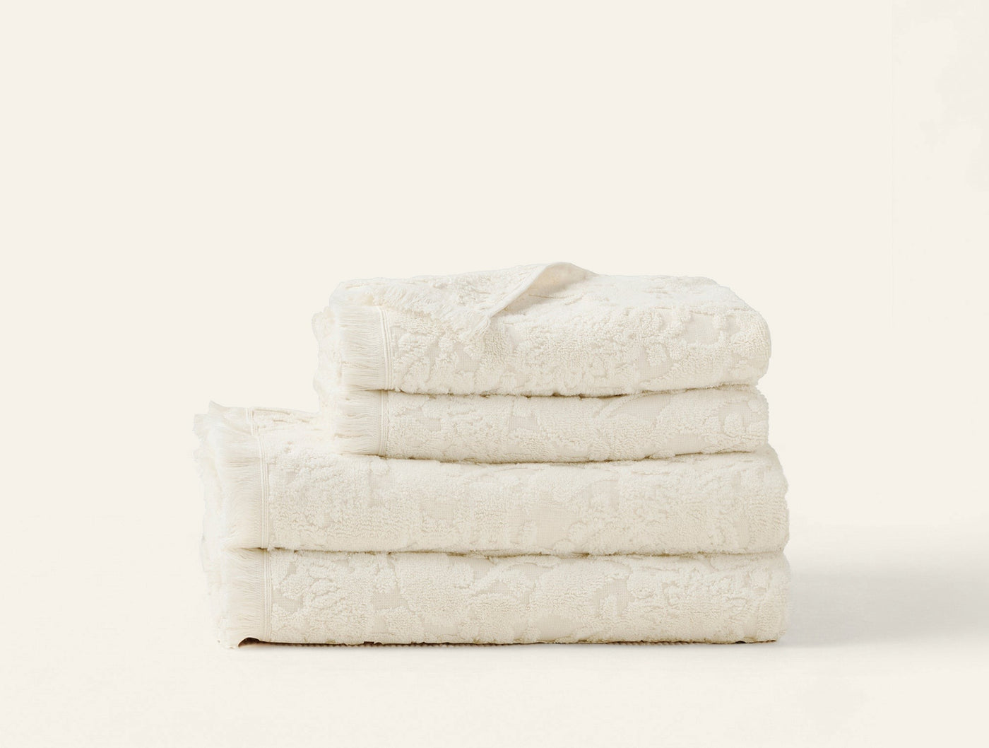 Stack of four ivory Coyuchi Wildflower towels showing floral jacquard texture, folded neatly.