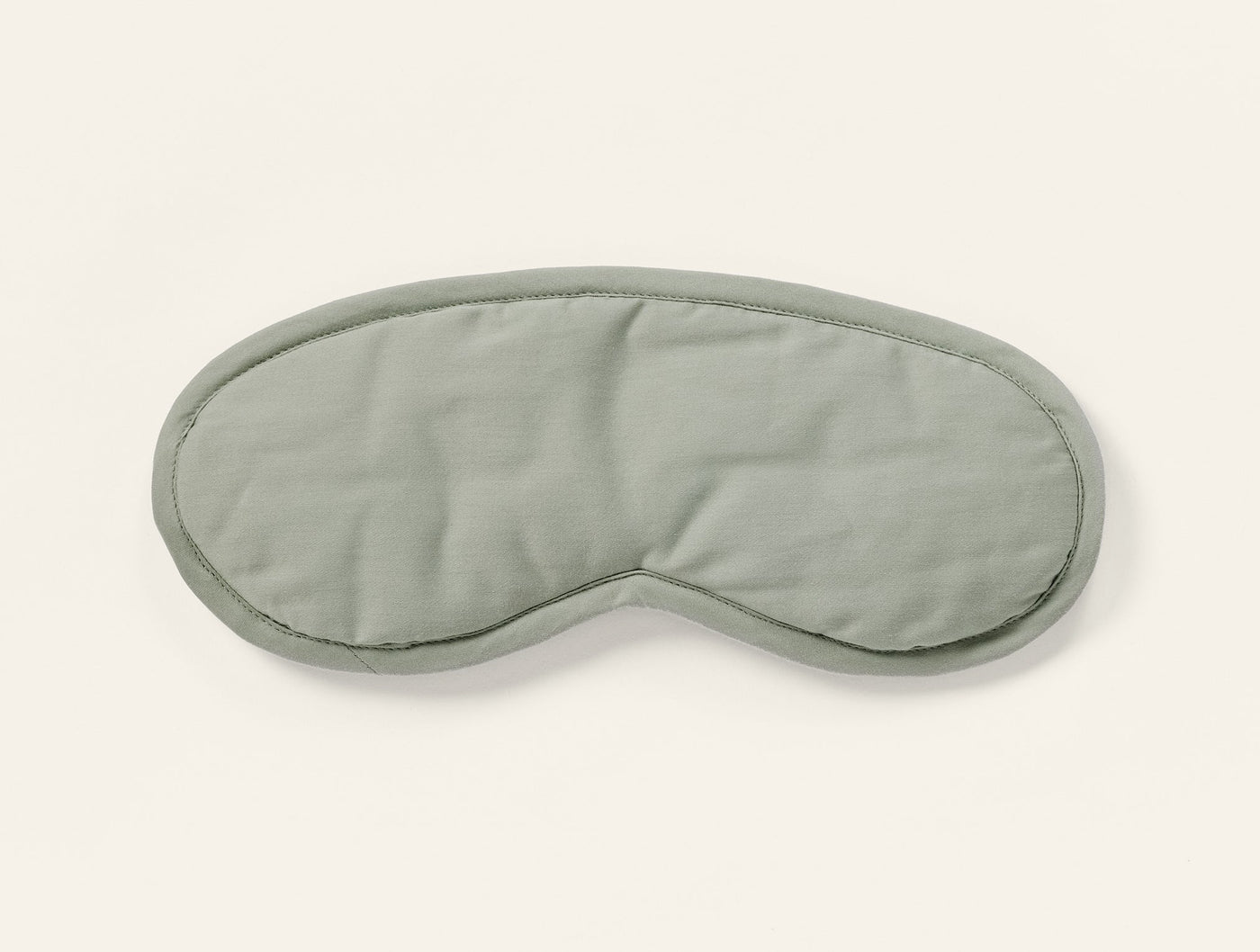 Sage green sateen eye mask with contrast piped edge, front view on white background.