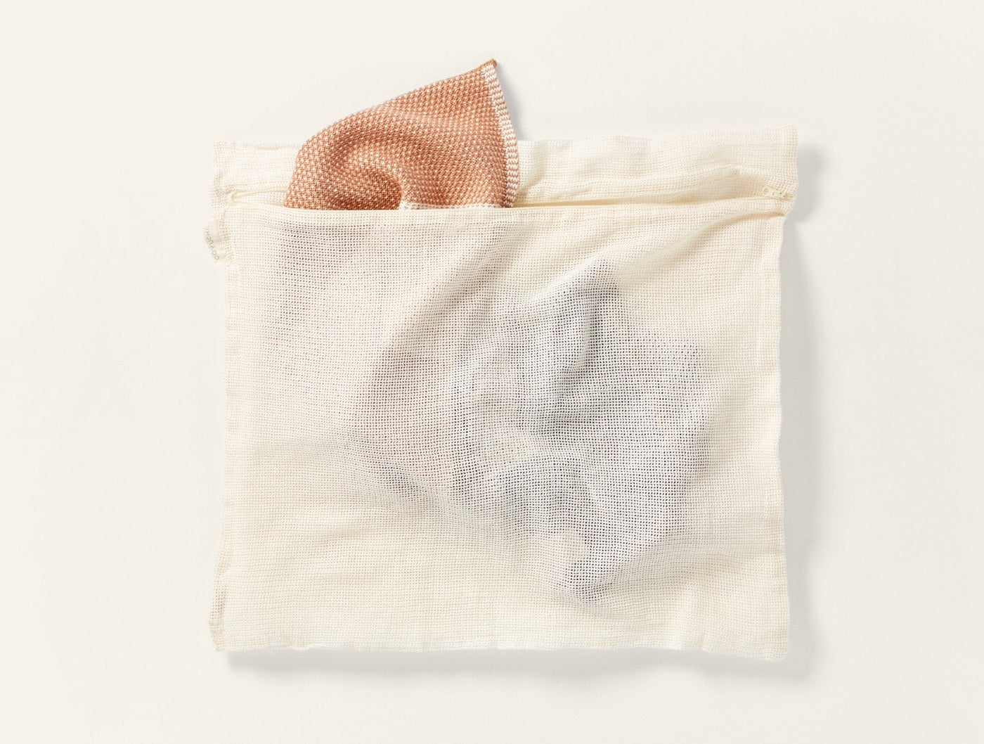 Coyuchi Conserve mesh laundry bag in natural, with a blush washcloth tucked inside.