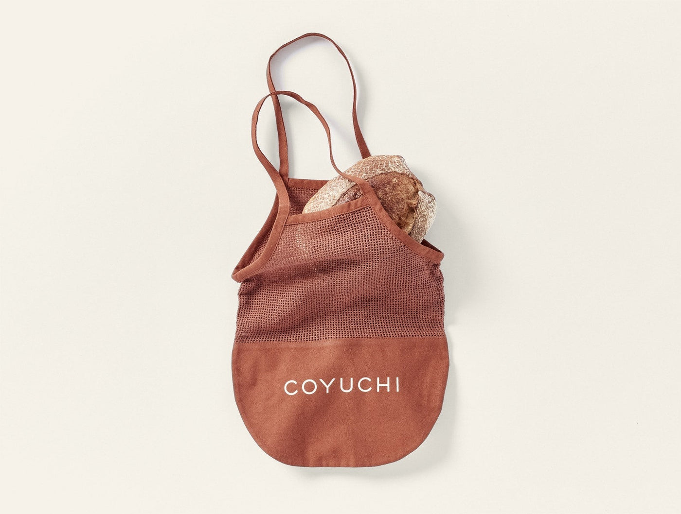 Coyuchi Conserve tote bag in terracotta mesh with canvas base, filled with bundled linens.