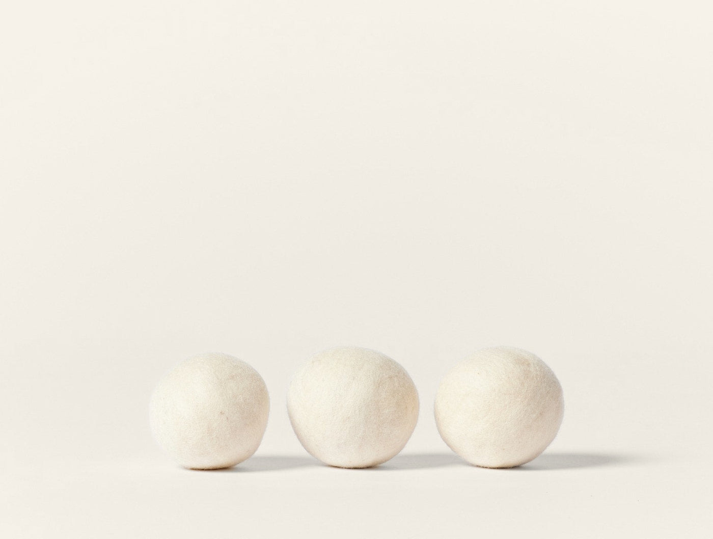 Coyuchi Felt Dryer Ball Set, three ivory wool balls on white background.