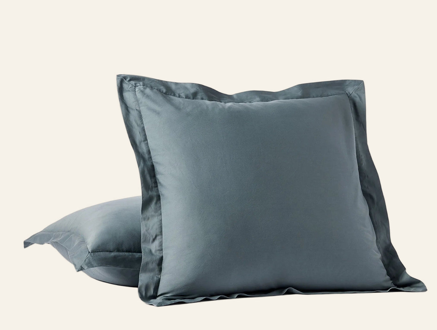 Two slate blue Coyuchi Cloud Soft Sateen shams stacked, front sham showing tailored flange border.