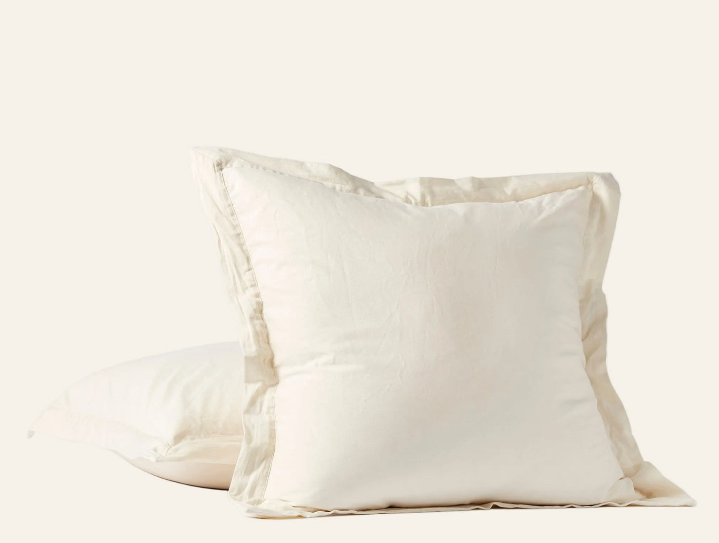 Close-up of two ivory Coyuchi Cloud Soft Sateen pillow shams stacked, showing flange edge detail.