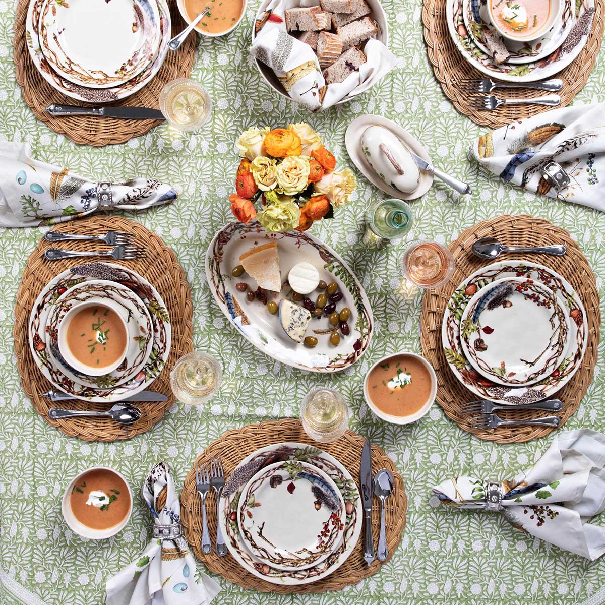 Overhead of a table set with Forest Walk dinnerware, soup, napkins and fruit on a green leaf tablecloth
