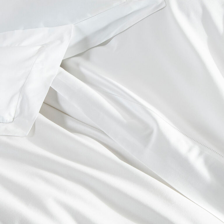 Frette’s Single Ajour | Sheet Set features neatly arranged white bed sheets and pillowcases in smooth, clean cotton sateen with natural folds and a refined open hemstitch finish.