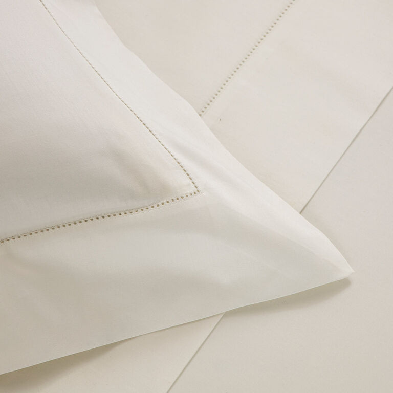 Close-up of the Frette Single Ajour Pillowcase Set in cream-colored cotton sateen, made in Italy, with elegant open hemstitch detail on smooth fabric.