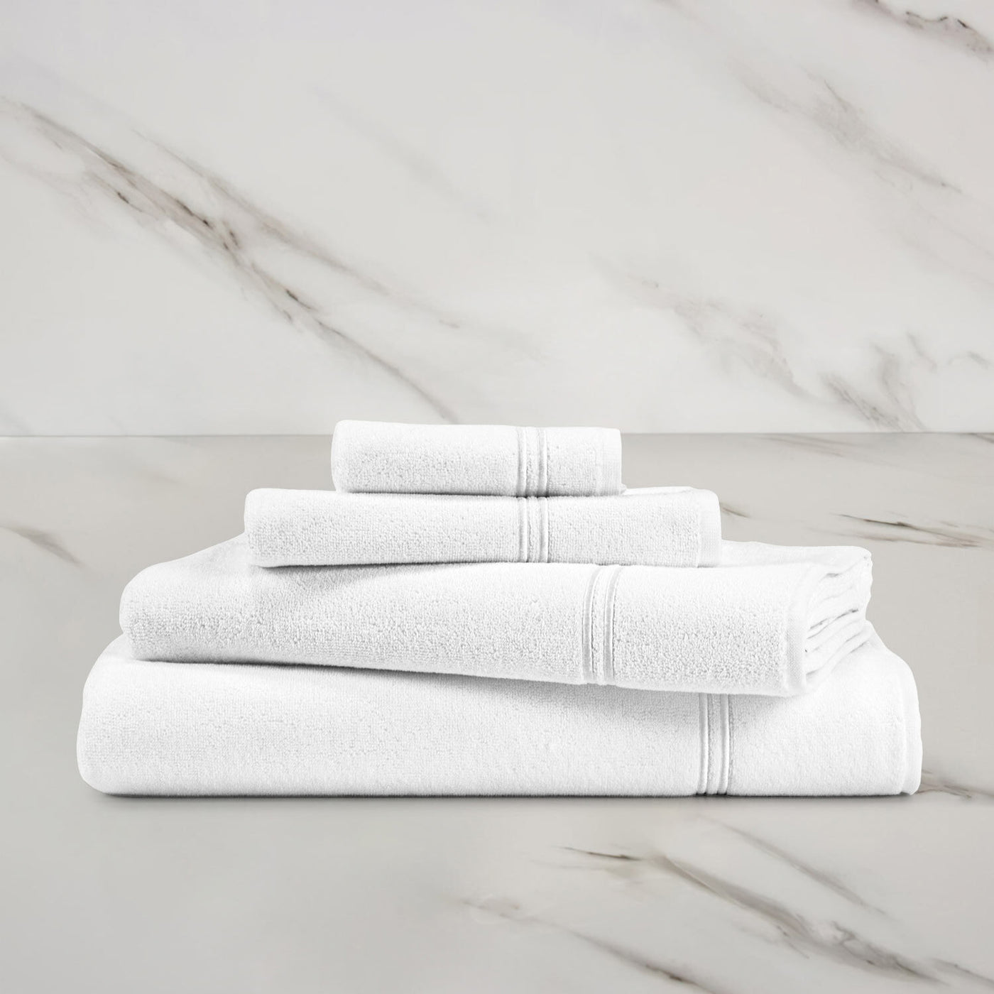 The Frette Classic Bath Sheet by Frette, a luxurious and absorbent white towel, is elegantly displayed on a marble surface against a marble wall backdrop.