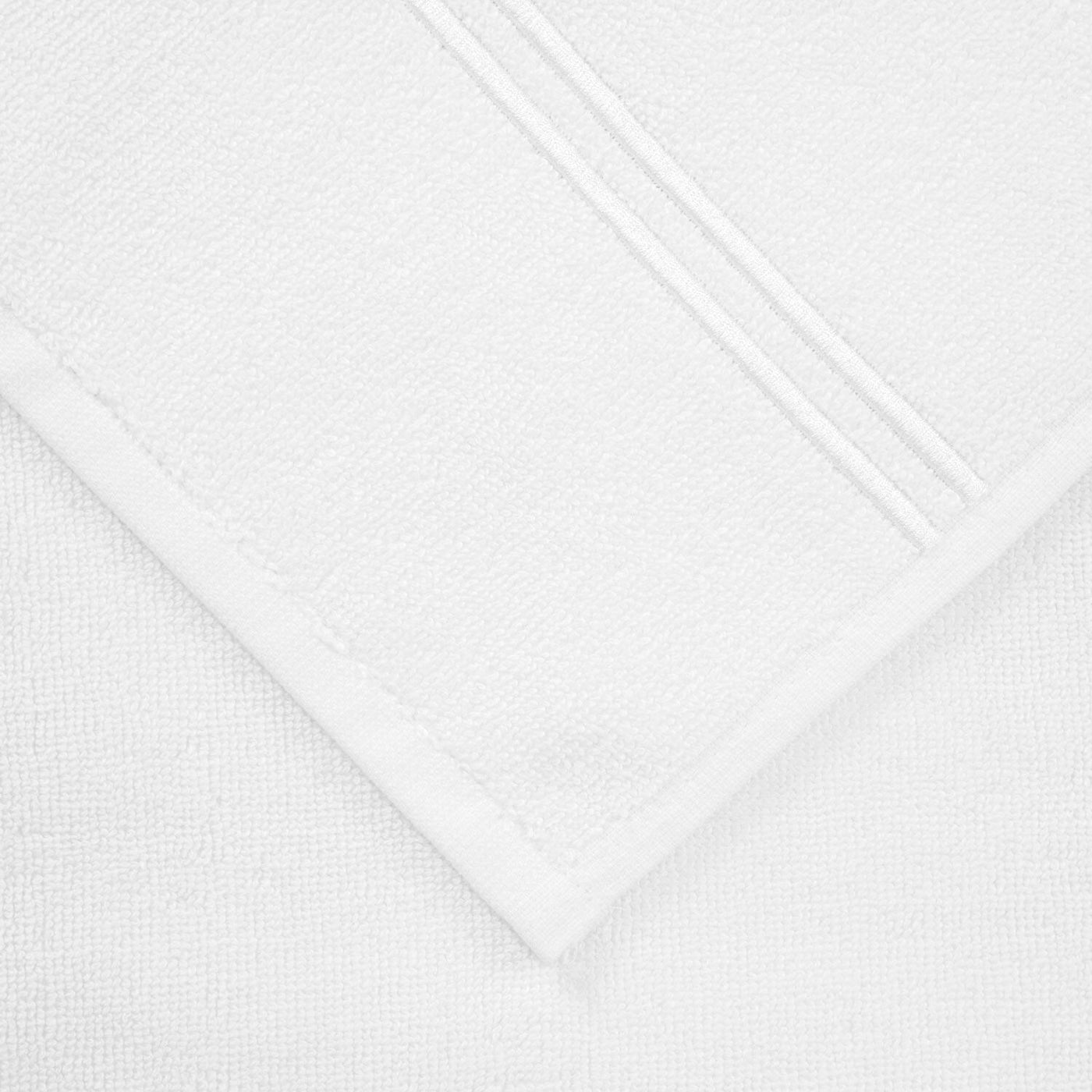 Close-up of the Frette Classic | Bath Mat by Frette, folded to display its subtle textured pattern and two parallel stitched lines near the edge, shown on a white background.