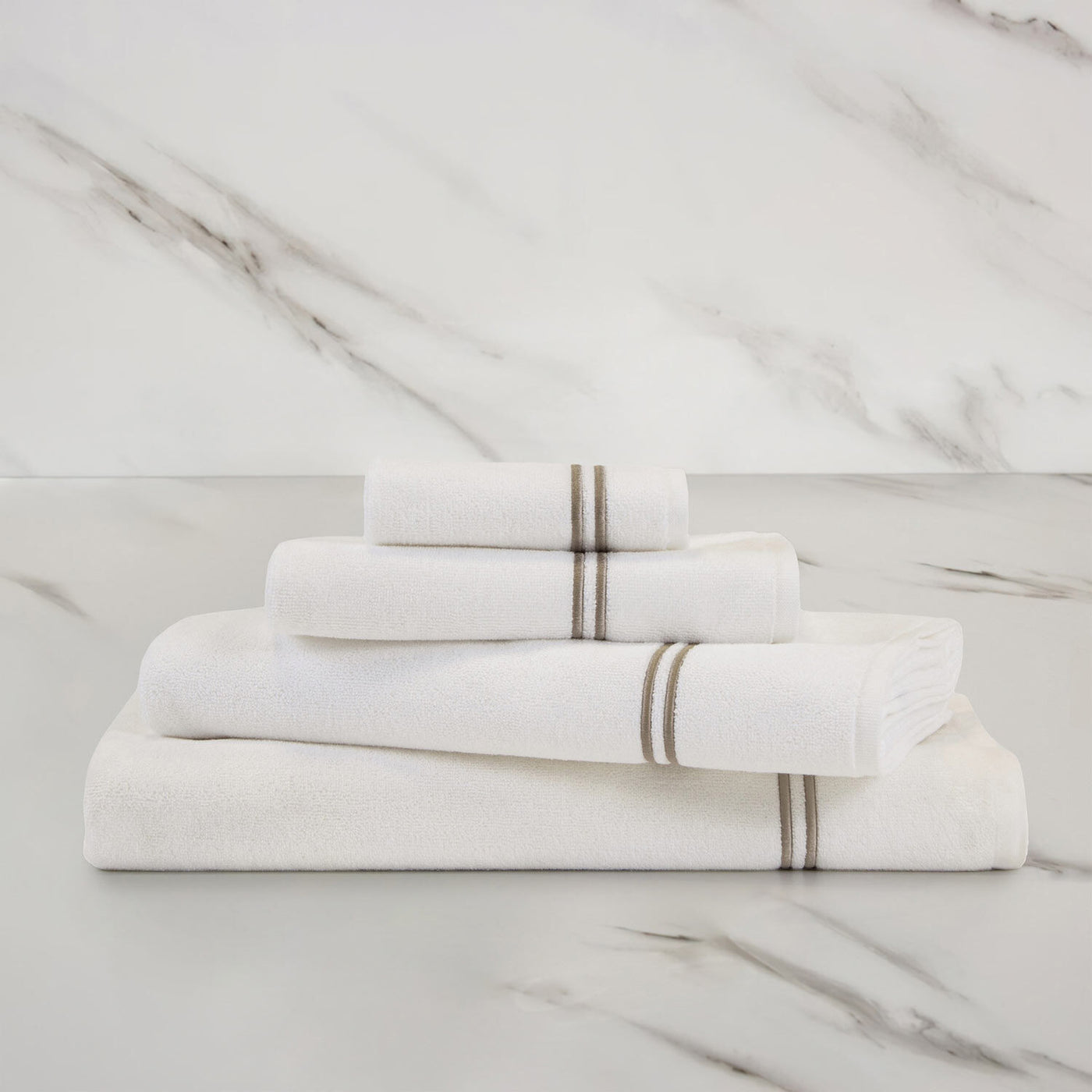 A neatly folded stack of Frette Classic | Hand Towels with gray stripes, by Frette, displayed on a marble surface against a marble background.