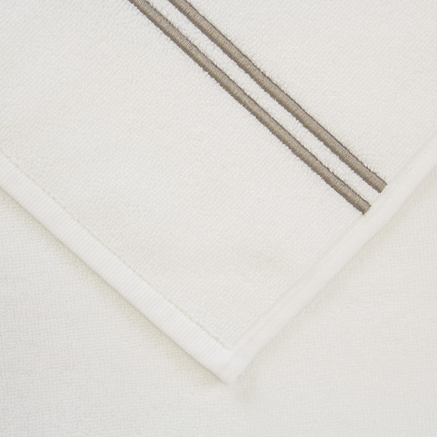 A close-up of the Frette Classic | Bath Sheet by Frette, featuring two parallel beige stripes near the edge, displayed on a plain background.