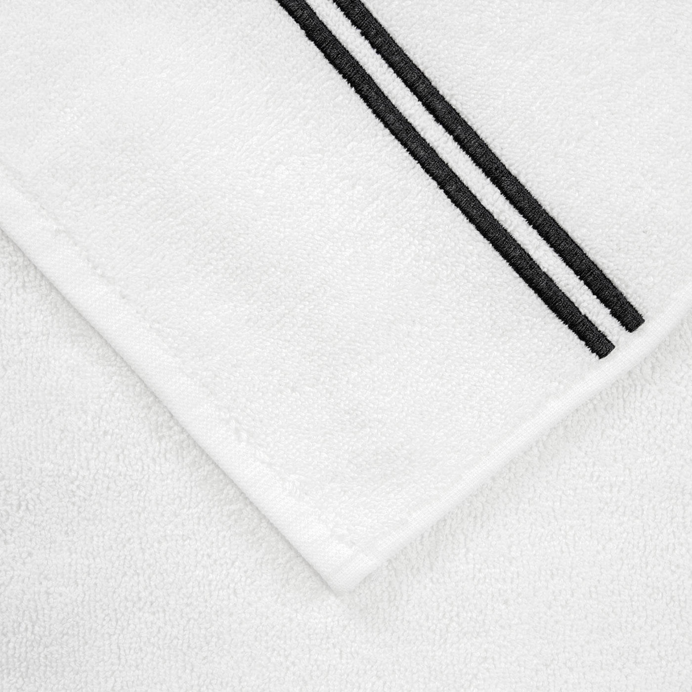 The Frette Classic Bath Mat by Frette features two parallel black stripes near one edge atop a crisp white background—a highly absorbent, elegant upgrade for any luxury bath collection.