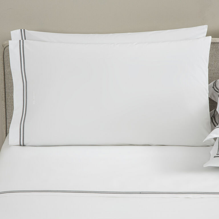 A neatly made bed with two white Frette Classic Pillowcase Sets, featuring gray-striped edges, and matching white cotton percale bed linens.