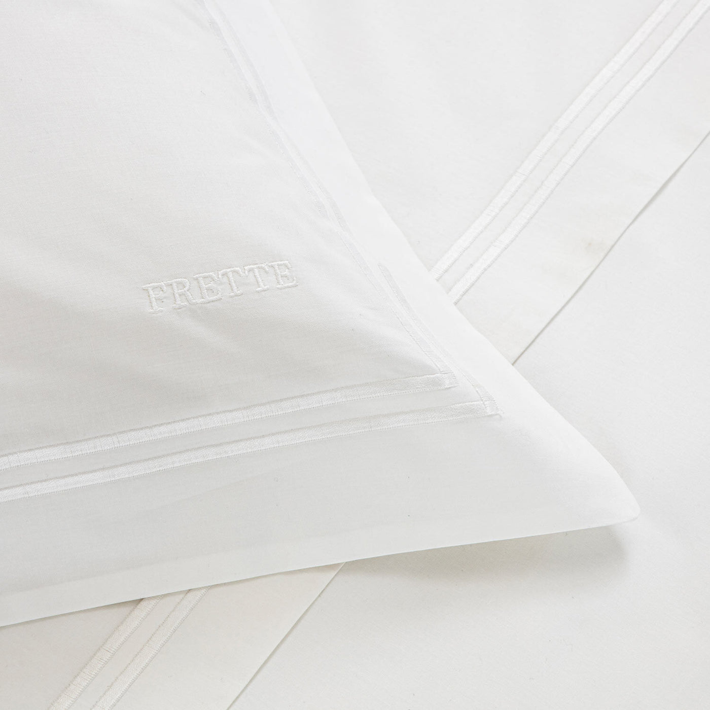A close-up of the Frette Classic Duvet Cover, featuring elegant borders and FRETTE embroidery, shown resting on a matching white cotton percale sheet.