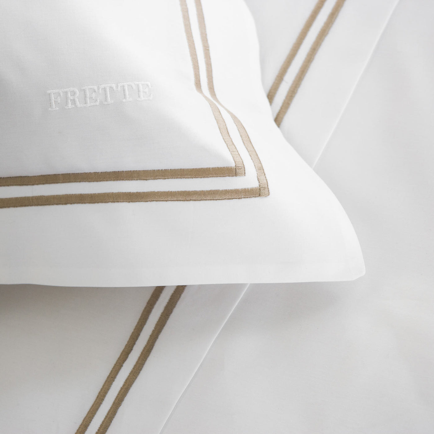 Close-up of the Frette Classic Duvet Cover, crafted from premium cotton percale with tan double borders and embroidered FRETTE logo, offering a luxurious bedding experience.