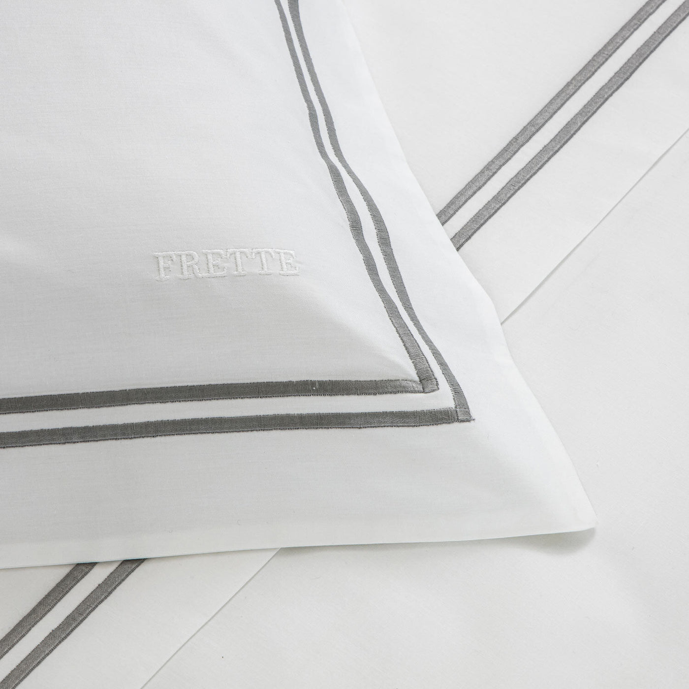 The Frette Classic Duvet Cover features white cotton percale with double grey borders and FRETTE embroidered on the fabric, offering a timeless touch of luxury.