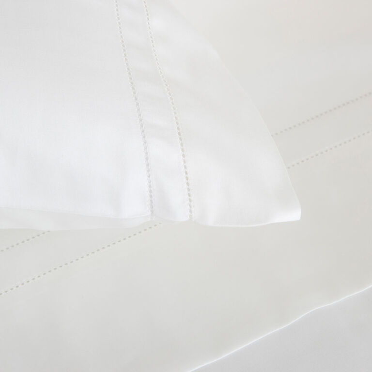 Close-up of the Doppio Ajour | Pillowcase Set by Frette in crisp cotton sateen, showcasing elegant decorative stitching and placed on a matching white bedsheet with coordinating stitched detail.