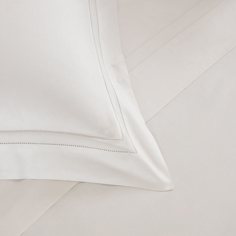 The Frette Doppio Ajour Pillow Sham, featuring a decorative stitched border, is displayed on coordinating white cotton sateen bed sheets.