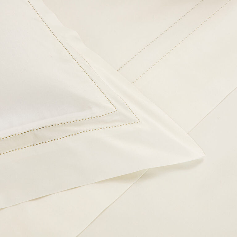 Close-up of cream-colored bed sheets and the Frette Doppio Ajour Pillow Sham, featuring subtle decorative stitching along the borders.