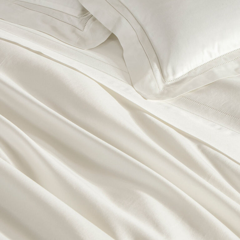 Close-up of a neatly made bed with Frette’s Doppio Ajour Duvet Cover in smooth, white cotton sateen, featuring elegant matching pillowcases and signature double open hemstitch detailing.