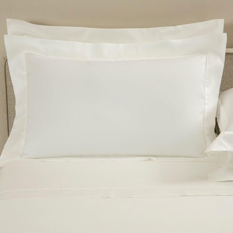 A neatly made bed with two stacked white Grace | Pillow Shams by Frette, featuring elegant shadow stitching on long-staple cotton sateen, set against a neutral headboard.