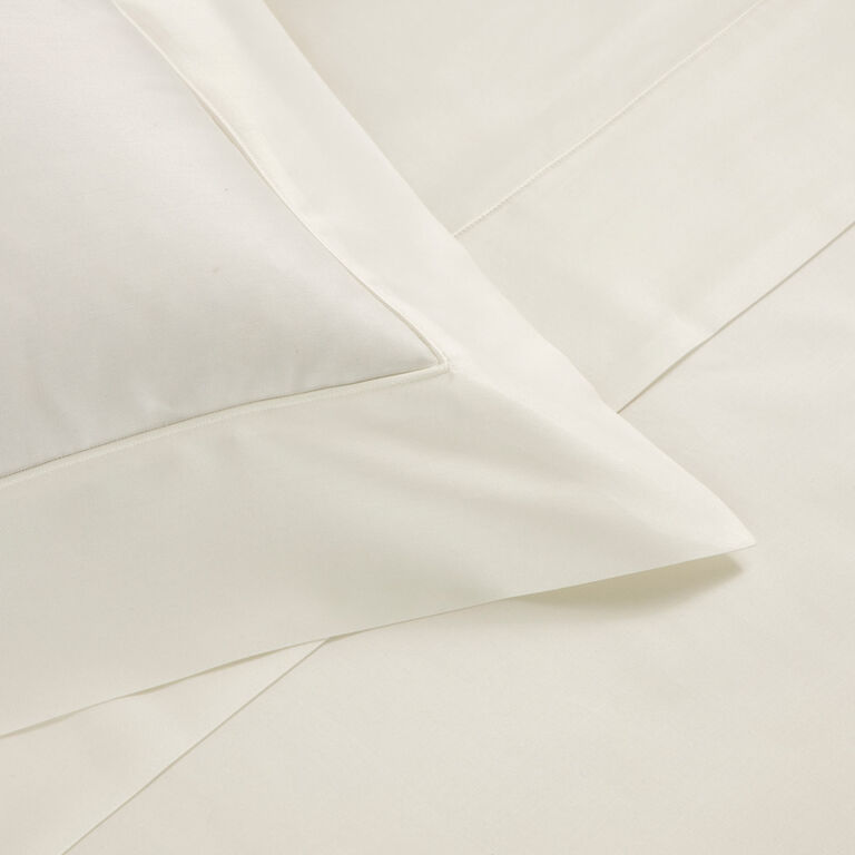 Close-up of a neatly made bed featuring the Grace | Duvet Cover by Frette, displaying smooth cream-colored long-staple cotton fabric and clean lines for an elegant, luxurious bedding look.