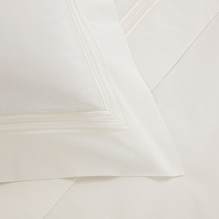 The Triplo Bourdon Pillow Sham by Frette features subtle three-line embroidery on white cotton poplin, offering a soft feel and high shine finish to complement your bed sheet.
