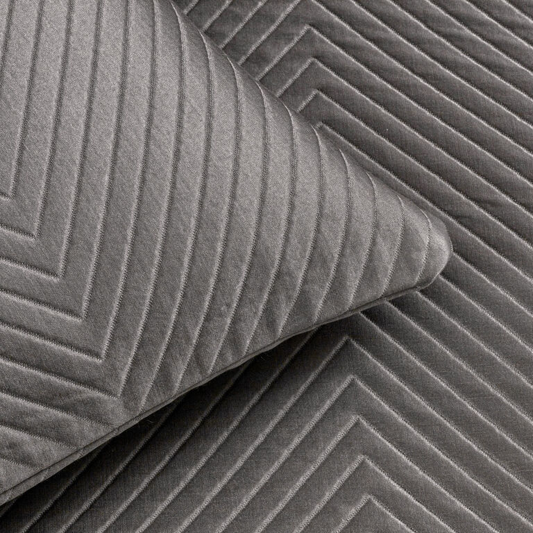 Close-up of two gray, quilted fabric surfaces with a chevron pattern, one overlapping the other—highlighting the refined texture of the Luxe Herringbone Decorative Sham by Frette.