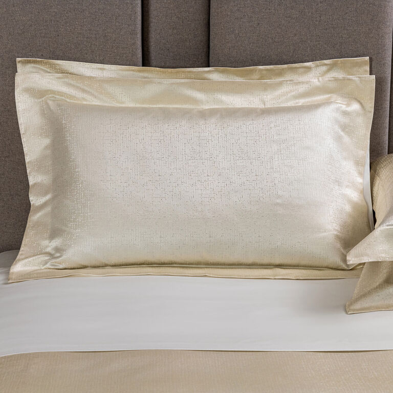 The Frette Luxe Glowing Weave | Sham, a cream-colored cotton silk jacquard satin pillowcase with a subtle textured pattern, is displayed on a neatly made bed with a padded gray headboard.