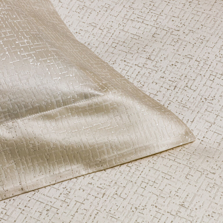 Close-up of the Luxe Glowing Weave | Duvet Cover by Frette—light beige cotton silk jacquard with a subtle geometric texture and a neatly folded corner, ideal for luxurious bedding.