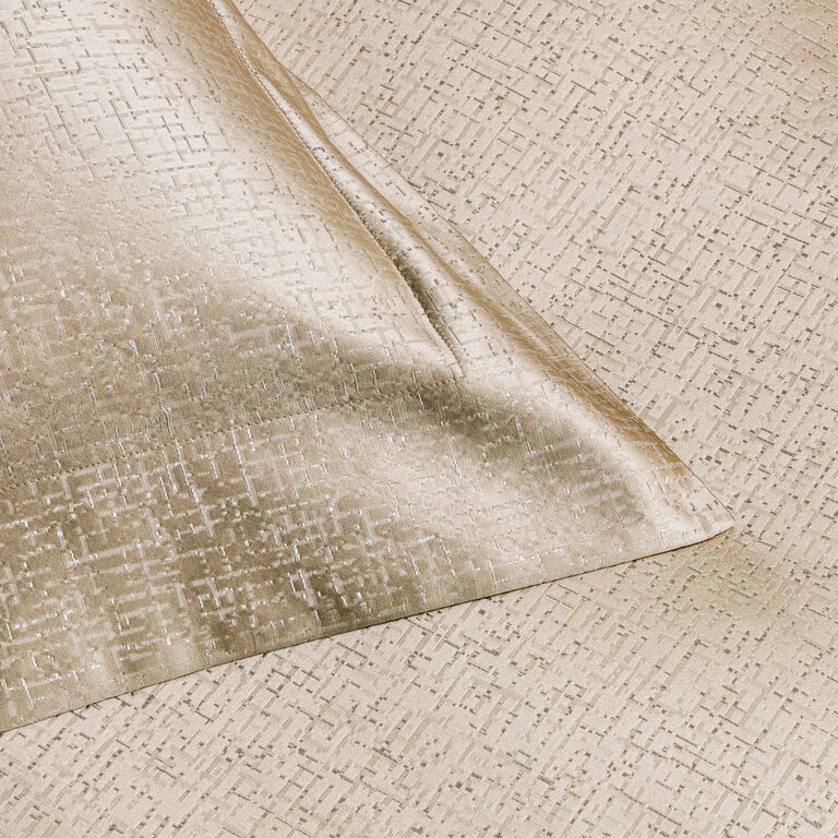 A close-up of Frette’s Luxe Glowing Weave | Sham in light gold cotton silk jacquard, featuring a subtle grid pattern on both a flat surface and a folded corner for a luxurious finish.