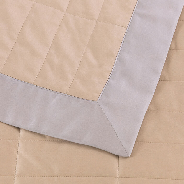 A close-up of the Frette Rectangular | Light Quilt in beige cotton sateen with a light gray border, showing the corner and stitched square pattern of this lightweight quilt.