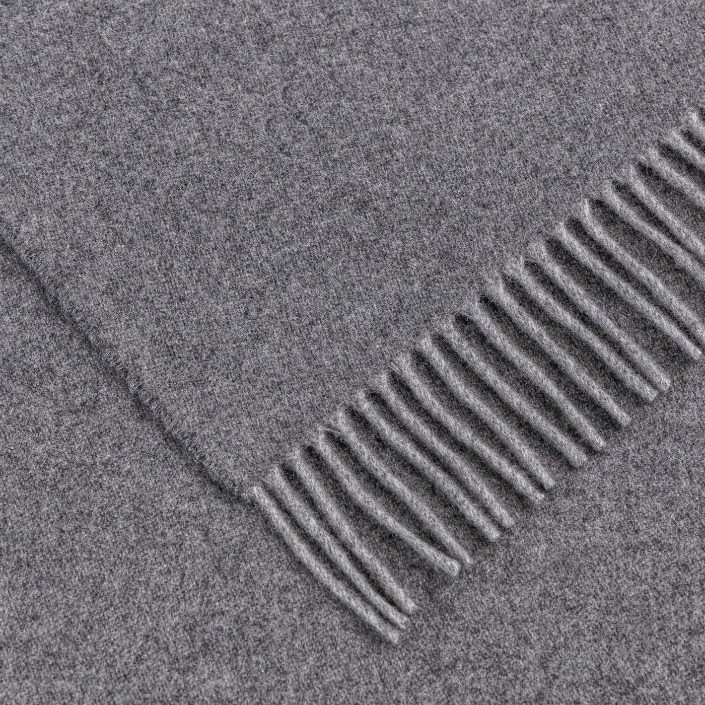 A close-up of The Pure Cashmere Throw by Frette, a folded gray cashmere piece featuring evenly spaced fringe on one end, made in Italy.