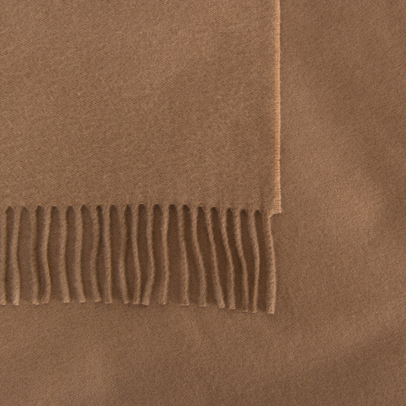 A close-up of Frette’s The Pure Cashmere Throw, featuring fringe ends, displayed on a coordinated brown fabric background.