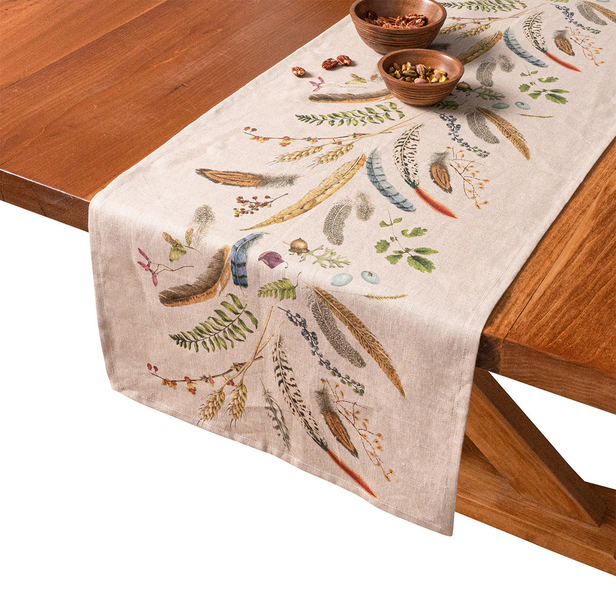Forest Walk 18 by 90 inch table runner with feather and fern print draped over a wooden table