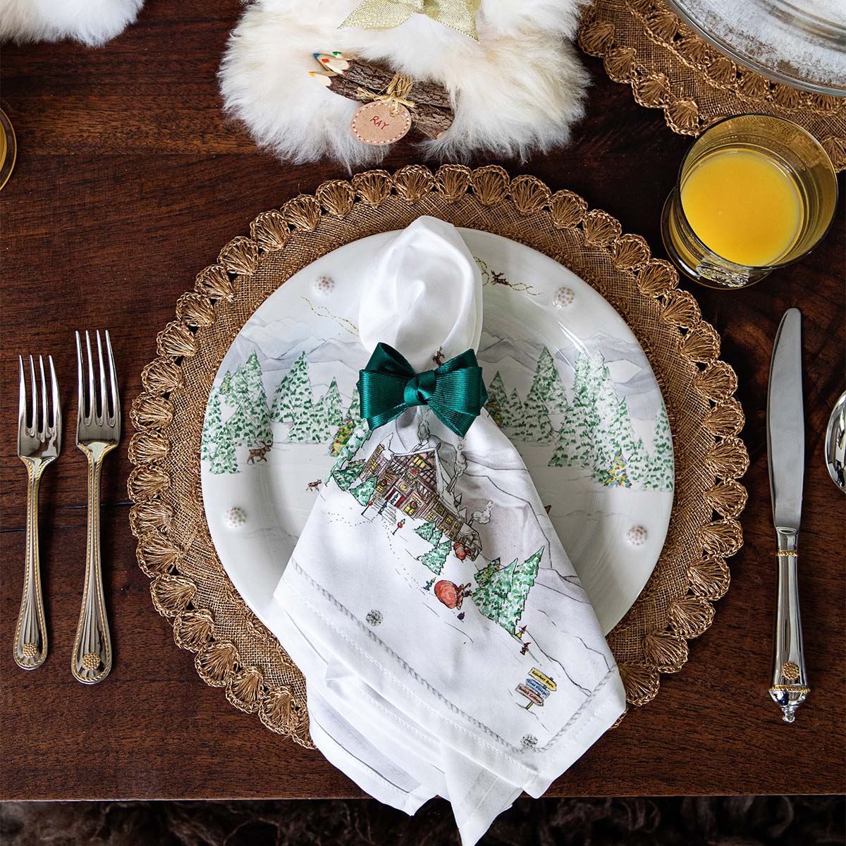 North Pole napkin with a green bow on a woven charger with silverware