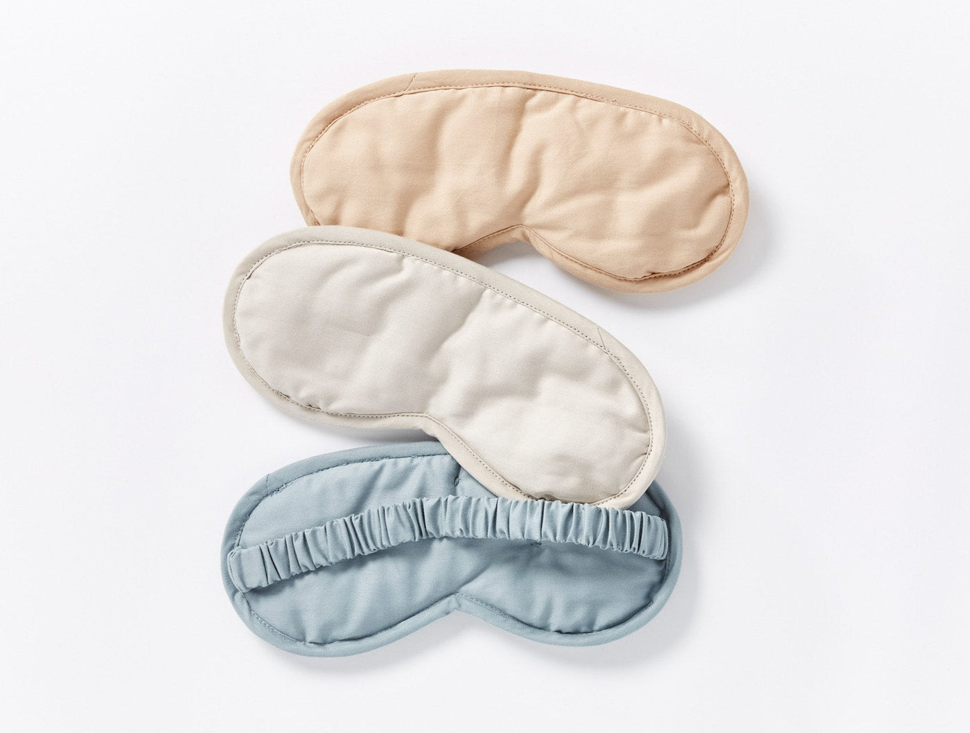 Three Coyuchi Cloud Soft Sateen eye masks in sand, ivory, and mist blue on white.