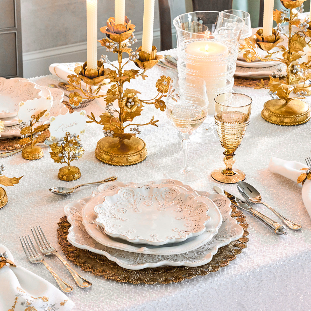 Gold holly place card holder among candelabras and scalloped plates on a white tablecloth