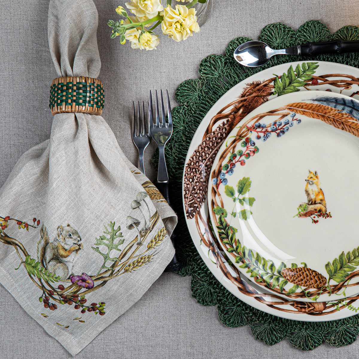 Forest Walk linen napkin in a ring beside stacked Forest Walk plates on a green charger